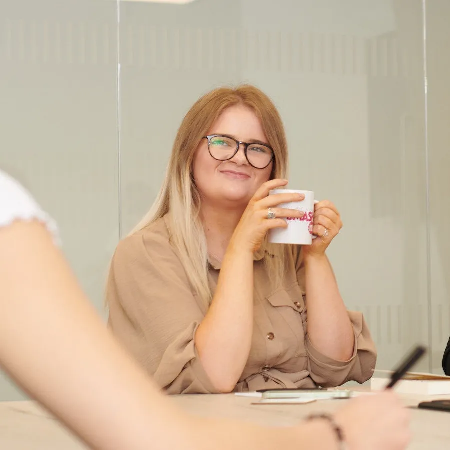 Rebecca Coles smiling in a meeting, holding a SMASH IT! mug.